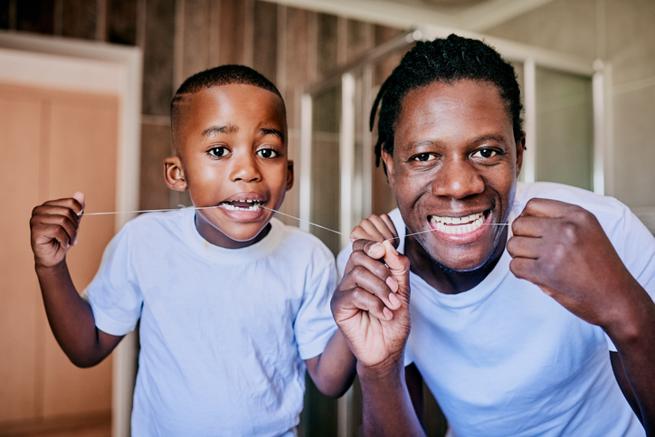 Man and his son flossing their teeth in the bathroom at home.